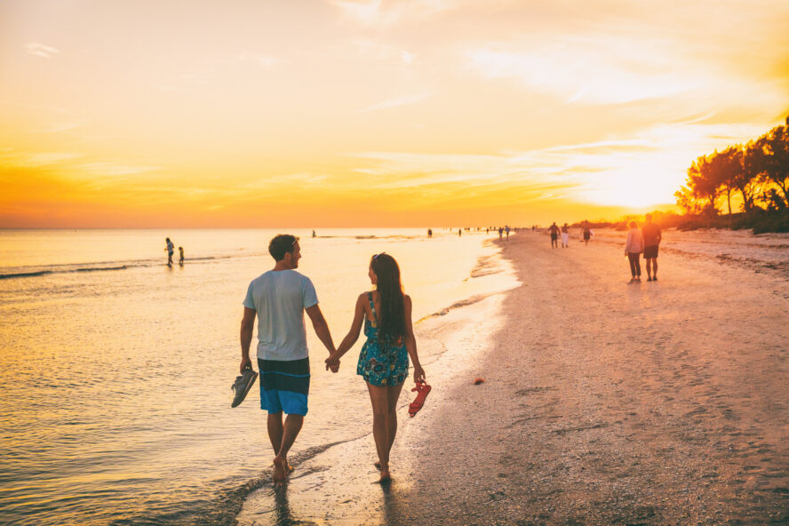 A man and woman holding hands on a beach.